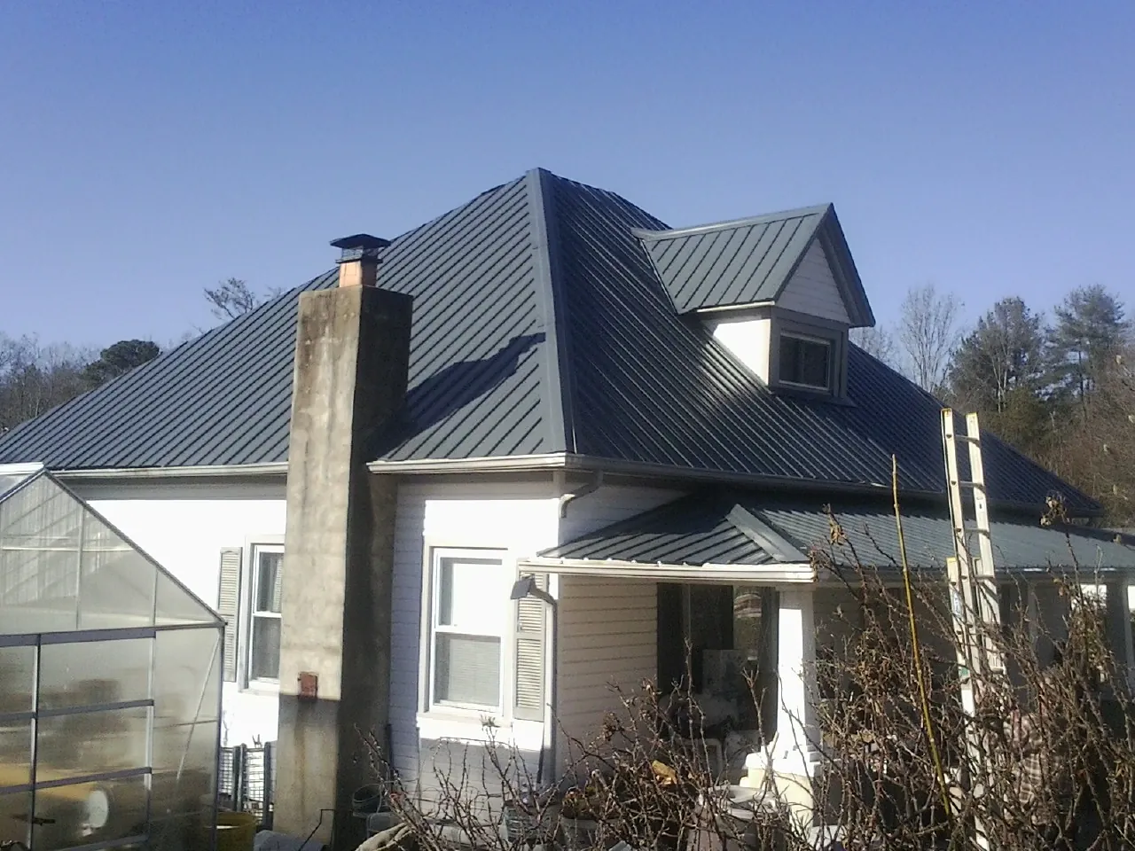 Dark blue standing seam metal roof on a white farmhouse with dormer — Slate & Tile Roof Repair by Roofing Brothers in Red Hill