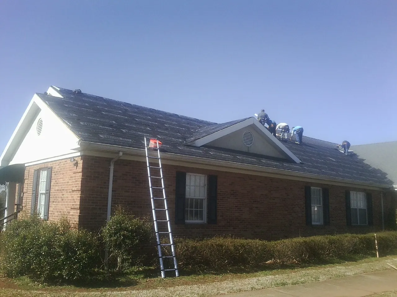Crew tearing shingles off a brick ranch roof with a ladder set — Metal Roof Repair work by our crew in Red Hill