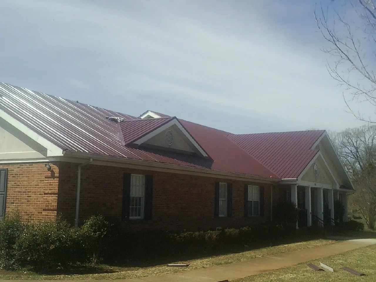 Red metal roof with gabled entries on a long brick building, from a Hail Damage Roof Repair job in Red Hill