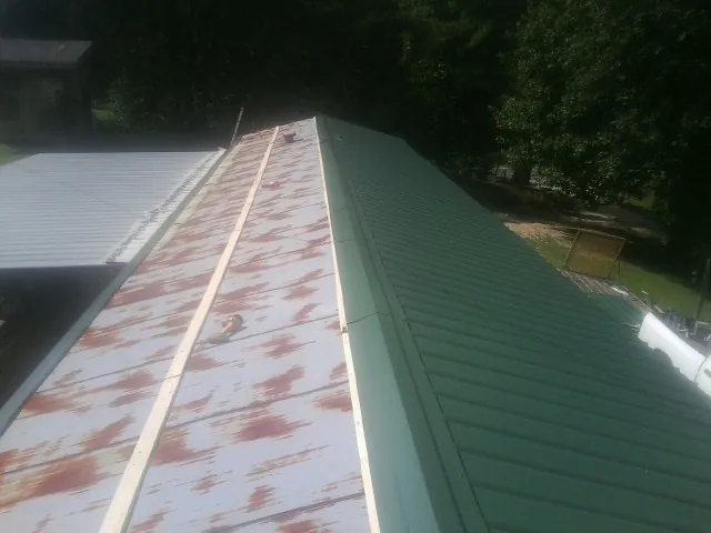 Old rusted panels beside newly installed green metal roofing — Wind Damage Roof Repair by Roofing Brothers in Red Hill