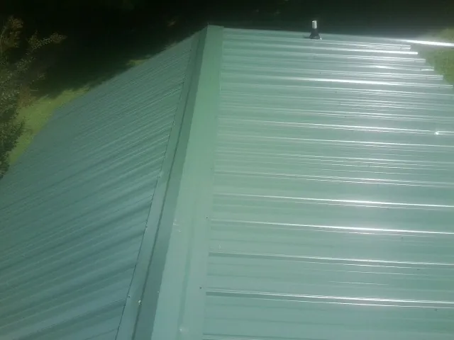 New green metal panels meeting at the ridge of a roof — Flat Roof Repair work by our crew in Red Hill