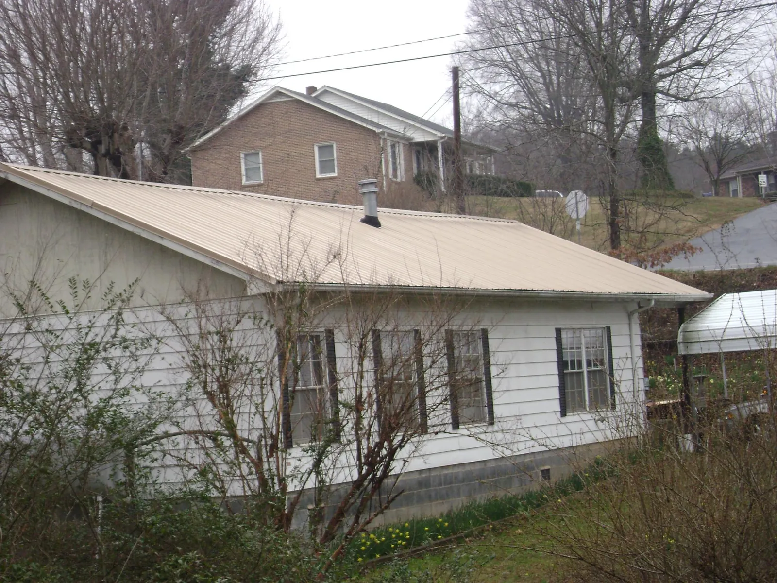 Tan metal roof on a white sided house set into a hillside — Commercial Roofing by Roofing Brothers in Red Hill