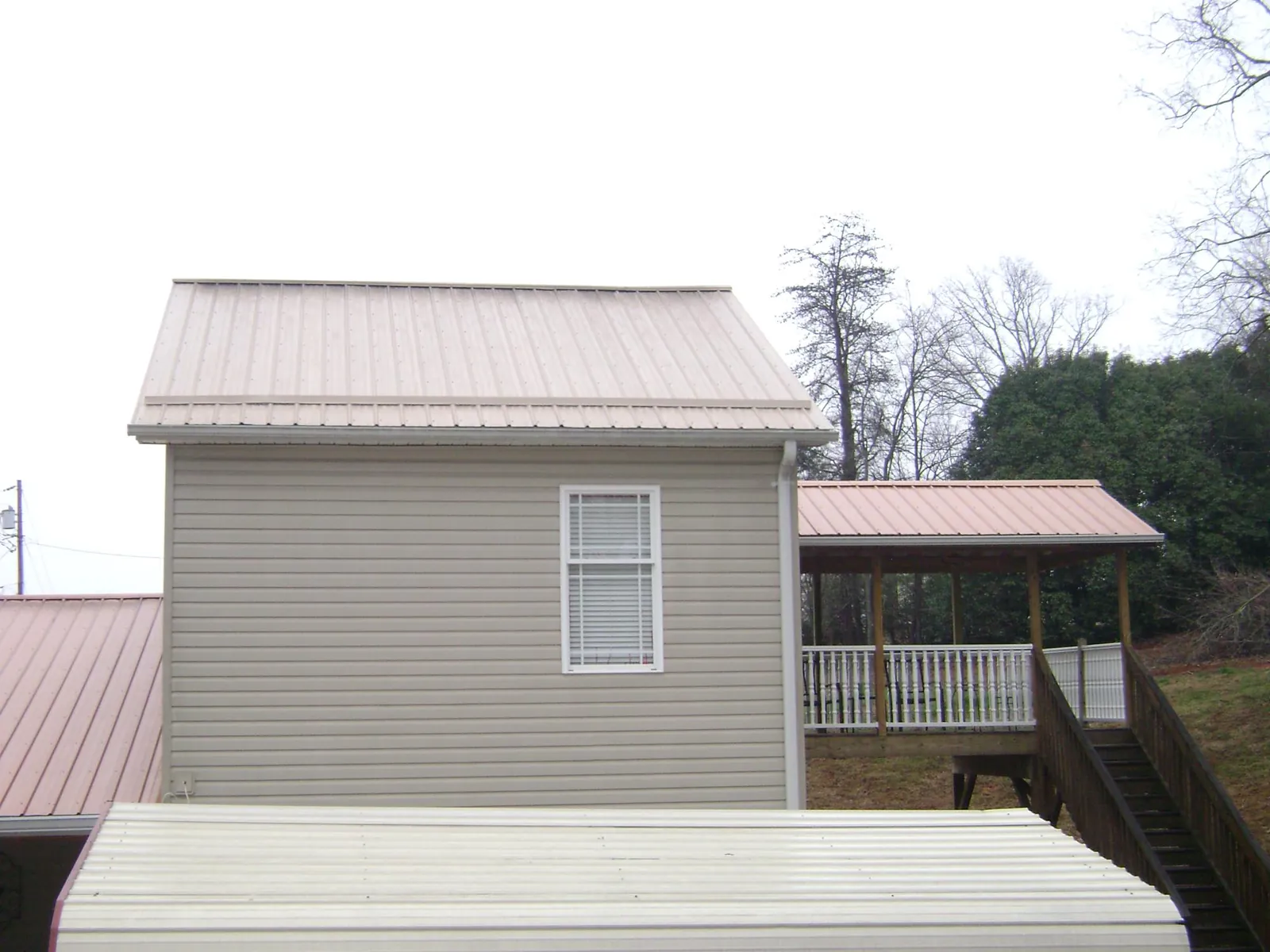 Tan metal roofs on a two story addition and attached porch, from a Roof Replacement job in Red Hill