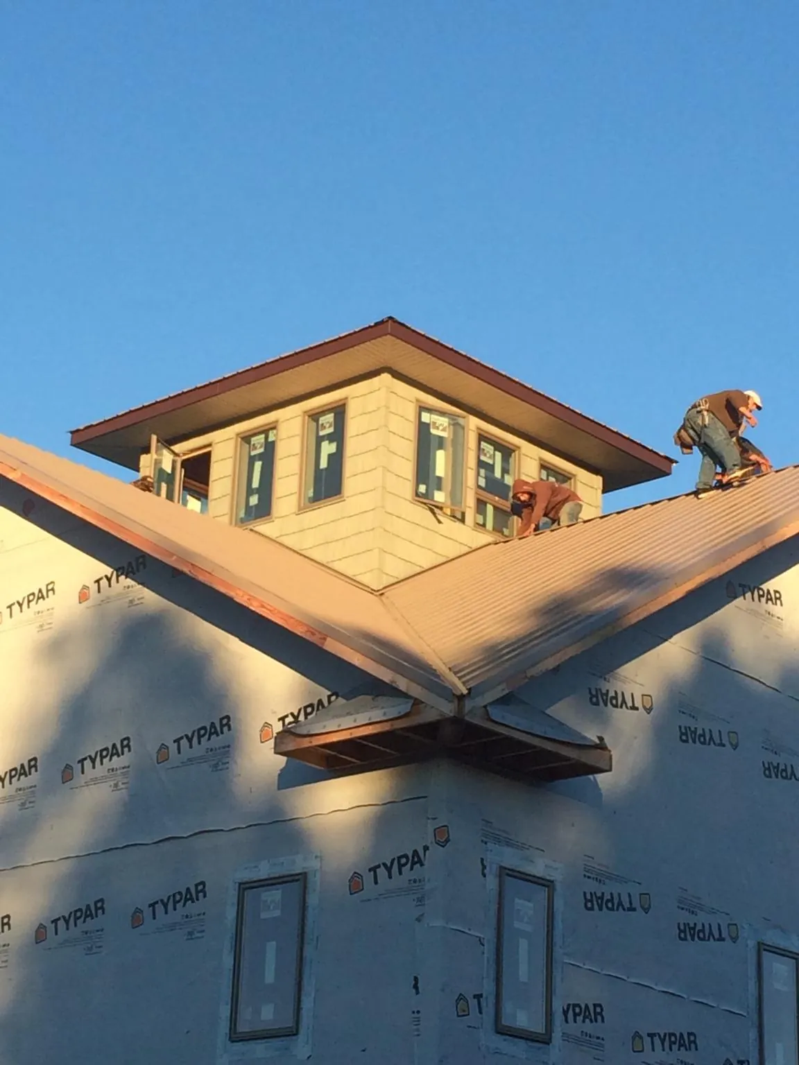 Roofers working around a rooftop cupola on a new metal roof at sunset — Roof Waterproofing in Red Hill by Roofing Brothers